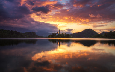 Obraz premium Dramatic sunrise on lake Bled, sunrise view on Bled lake, island, Pilgrimage Church of the Assumption of Maria and Castle with mountain range (Stol, Vrtaca, Begunjscica). Bled, Slovenia,
