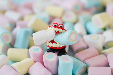 Fake teeth toy stand on a pile of colored candies and holds a marshmallow in its mouth