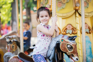 Adorable little toddler girl riding on animal on roundabout carousel in amusement park. Happy...