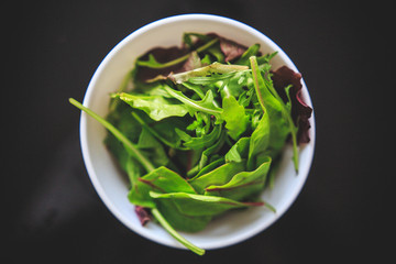 Fresh mixed salad with green and purple juicy color in the white bowl on black background taken from the top.