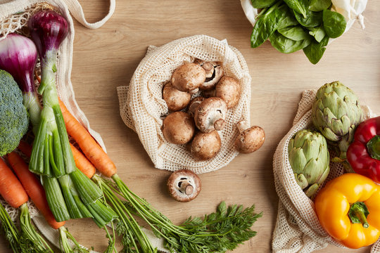 Raw mushrooms in reusable bag surrounded by fresh vegetables.