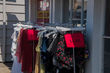 Rack of women's clothes with red blowout sale signs outside on a sidewalk in front of a clothing...