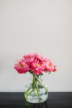 large glass vase filled with coral charm peonies sitting on a black table