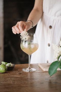 Crop woman adding elderberry flower in cocktail.
