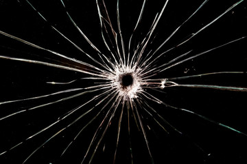 Obraz premium A bullet hole in glass. The background is black. Cracks radiate from the hole.