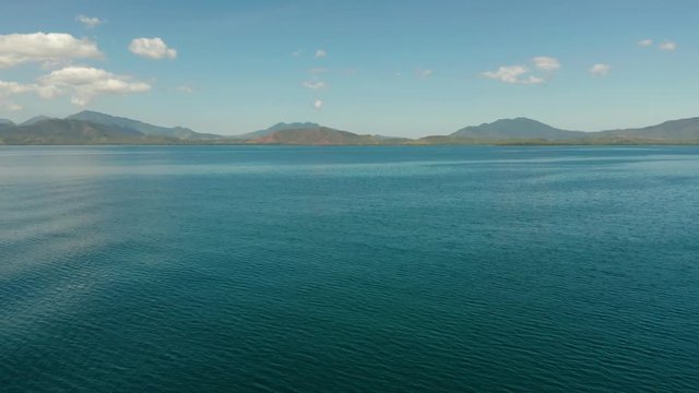 Flying over the surface of the blue sea to an island with mountains covered with forest. aerial view, seascape. Honda bay, Puerto princesa, Palawan, Philippines.