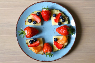 Various spring fruit on a turquoise plate: strawberries, pineapple, blueberries and tangerine. Top view.