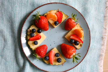 Various spring fruit on a turquoise plate: strawberries, pineapple, blueberries and tangerine. Top view.