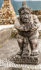 Fototapeta na wymiar Bali, Indonesia - February 25, 2019: Ulun Danu Beratan Temple complex in Bedoegoel. Gray stone statue of dwarf in park.