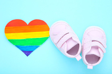 Rainbow paper heart with baby shoes on blue background