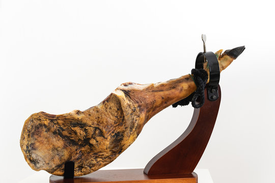 Spanish delicatessen dry cured meat ham, whole leg, jamon iberico bellota on jamonero stand selective focus - white background
