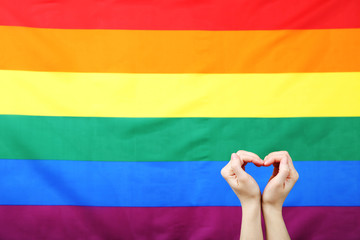 Female hands in shape of heart on rainbow flag background