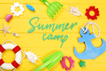 Paper text Summer camp with seashells and plastic toys on yellow wooden table