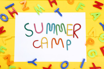 Text Summer camp with plastic letters on yellow wooden table