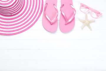 Pair of flip flops with starfish, glasses and hat on white wooden table
