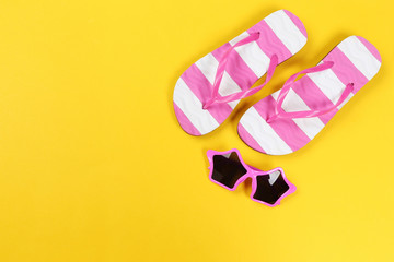 Pair of flip flops with sunglasses on yellow background