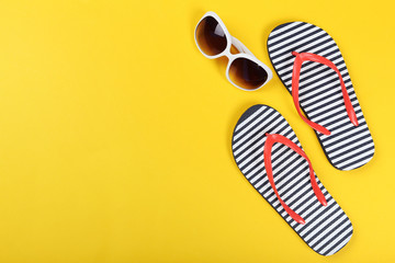 Pair of flip flops with sunglasses on yellow background