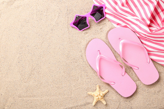 Pair of flip flops with starfish and sunglasses on beach sand