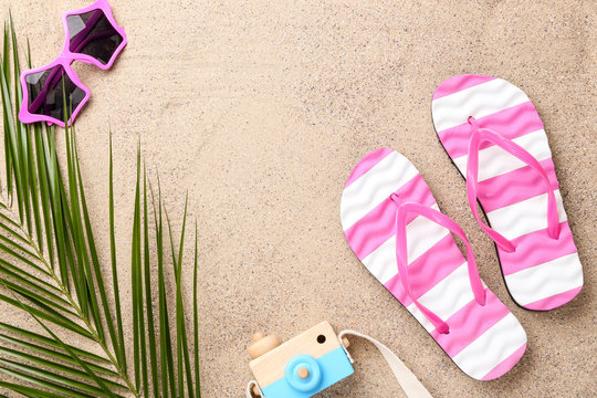 Pair of flip flops with sunglasses and palm leaf on beach sand