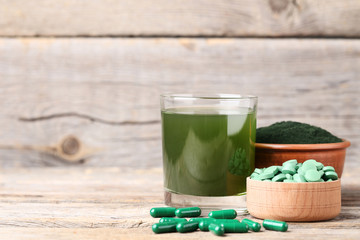 Spirulina drink and pills with powder in bowl on grey wooden table