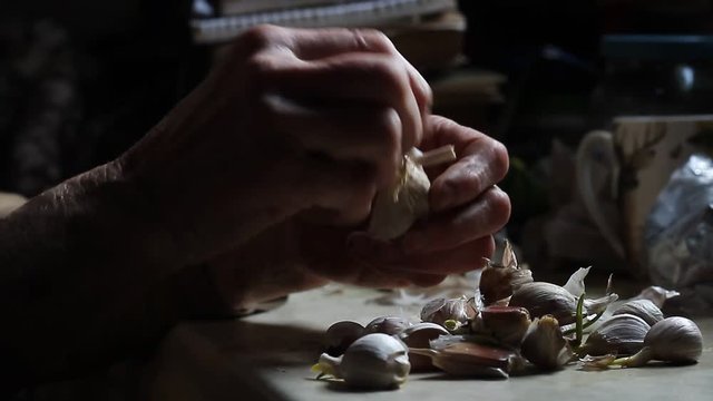 The hands of a sick old woman clean and touch the heads of garlic before cooking in the old rustic kitchen, selective focus