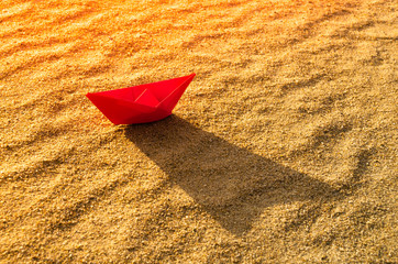 Red paper boat at the bottom of a dry sea. Beach, heat and vacation.Ecology, drought.