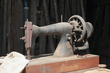 Old sewing machine, with manual drive. Covered with corrosion, dust and cobwebs. A piece of coarse fabric is sewn into it.