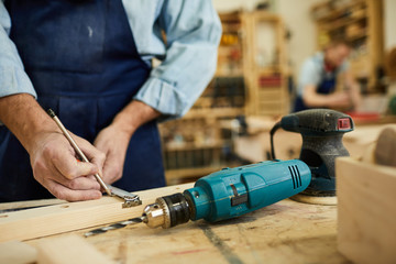 Closeup of mature carpenter working with wood standing at table in workshop, copy space