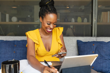 Smiling businesswoman looks at phone in front of laptop