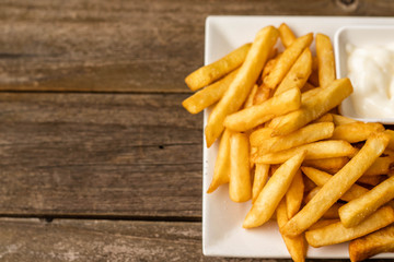 French fries fast food,french fries amount many pieces and mayonnaise, in dish square white all place on wooden table.