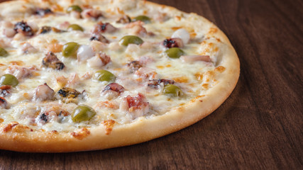 Pizza with olives and seafood on a wooden table close-up.