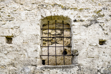 Arched window with metal bars in old stonework. The ancient half-ruined synagogue.