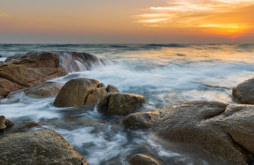 The rock and smooth sea wave in the sunset time.