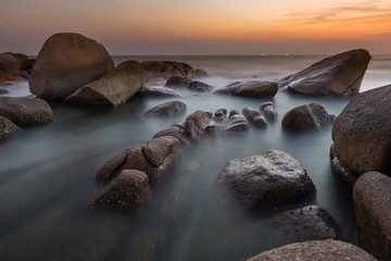 The rock and smooth sea wave in the sunset time.