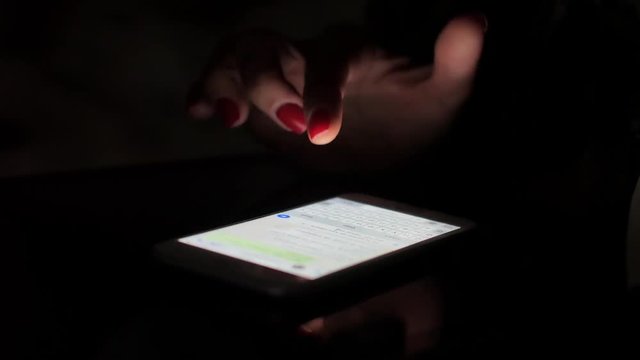 Girl in the dark is typing on a smartphone