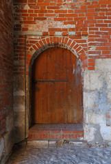 Fototapeta na wymiar Brown wooden door with padlock in the medieval red brick wall St. Nicholas Gate Tower of the Zaraysk Kremlin