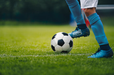 Close up of legs and feet of football player in blue socks and shoes running and dribbling with the ball. Soccer player running after the ball. Sports venue in the background - Powered by Adobe