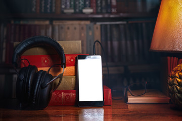 Mobile phone, headphones and a stack of books near the lamp on a wooden table. Concept of training...