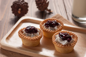 Delicious homemade mini berry tarts and custard on wood cutting board