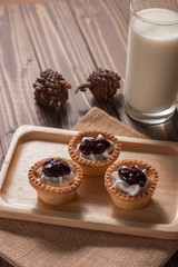 Delicious homemade mini berry tarts and custard on wood cutting board