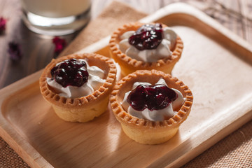 Delicious homemade mini berry tarts and custard on wood cutting board
