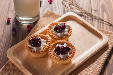 Delicious homemade mini berry tarts and custard on wood cutting board