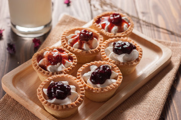 Delicious homemade mini berry tarts and custard on wood cutting board
