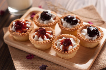 Delicious homemade mini berry tarts and custard on wood cutting board