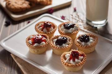 Delicious homemade mini berry tarts and custard on wooden cutting board