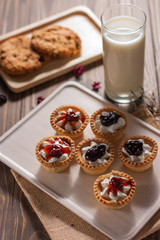 Delicious homemade mini berry tarts and custard on wooden cutting board