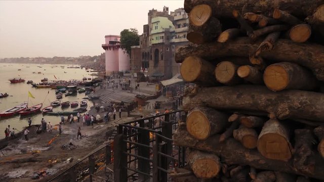 Wide panoramic still shot facing Ganga River from the top of an old Varanasi building, of the sacred cremation ground, and piled firewood at Markarnika Ghat, Varanasi, India