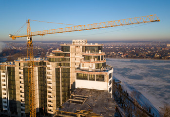 Fototapeta na wymiar Apartment or office tall building under construction, top view. Tower crane on bright blue sky copy space background, city landscape stretching to horizon. Drone aerial photography.