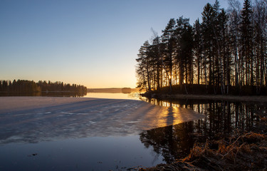 Sunset behind the forest on a lake shore. Wintry landscape, beautiful scenery.
