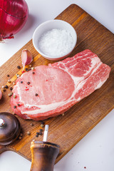 Raw pork steak with a bunch of thyme, garlic, salt, pepper and onion on a wooden cutting board top view.